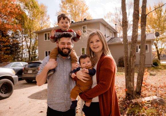 young couple with young children standing in front of their home in fall
